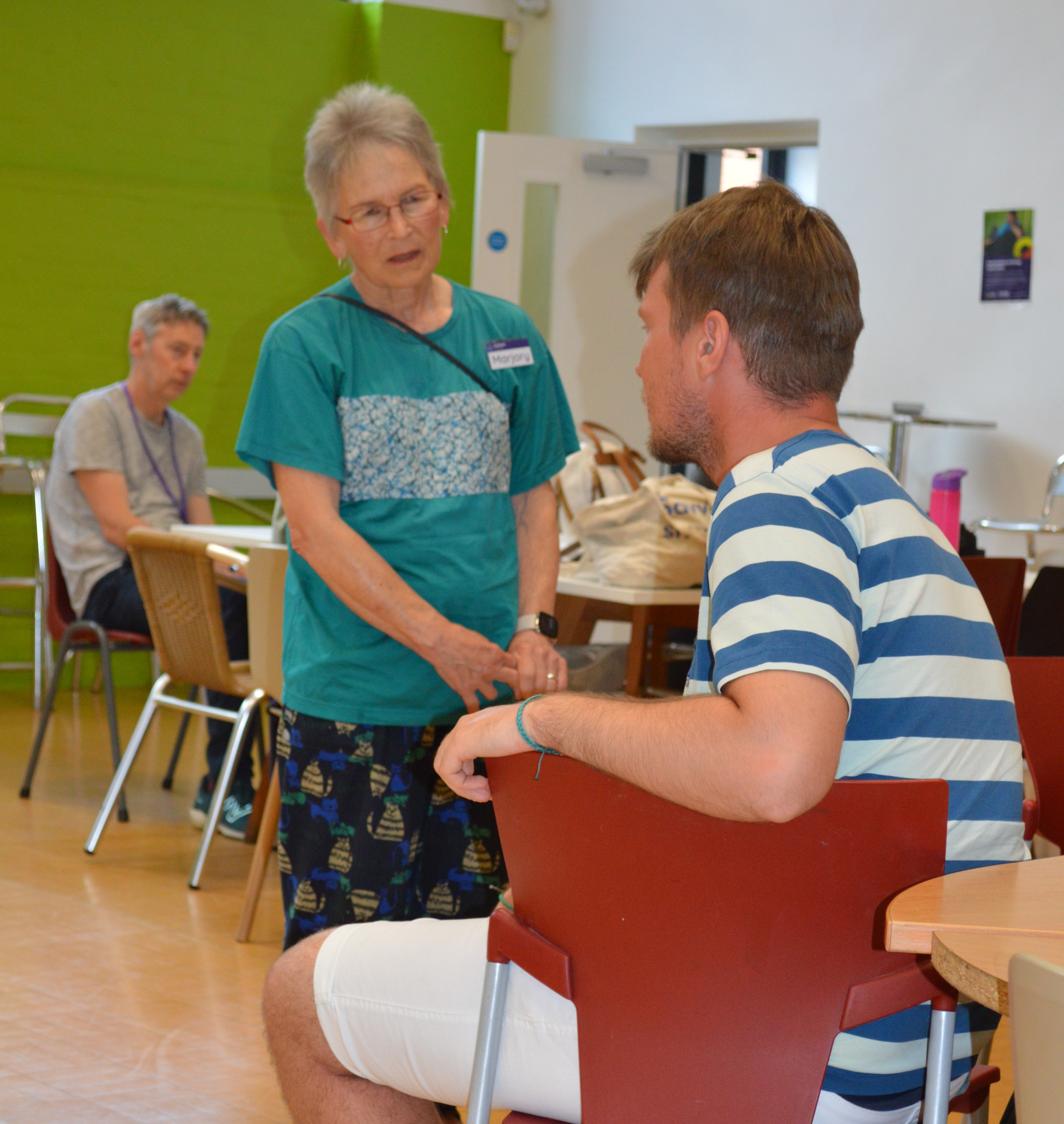 Marjory stands at the Eastleigh group listening to one of the members in a blue and white striped top.